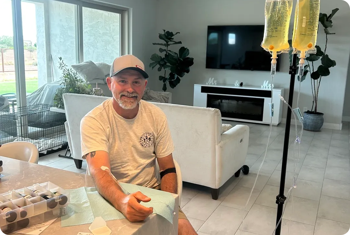 Smiling man receiving IV treatment in a bright living room.