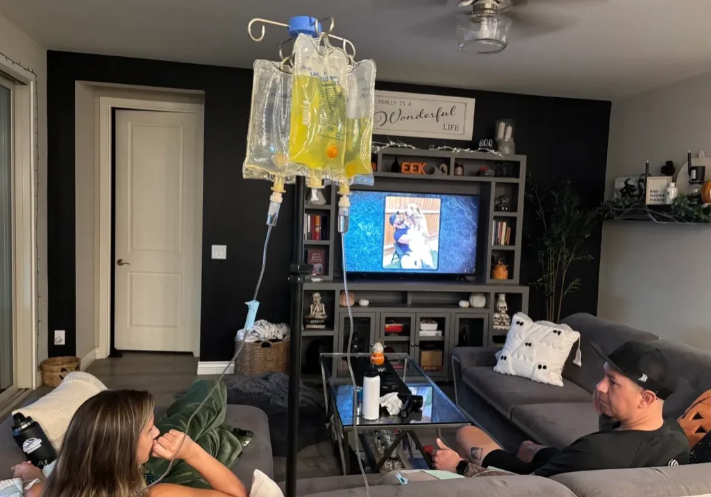 Two people relaxing in a living room with a TV and an IV drip stand.